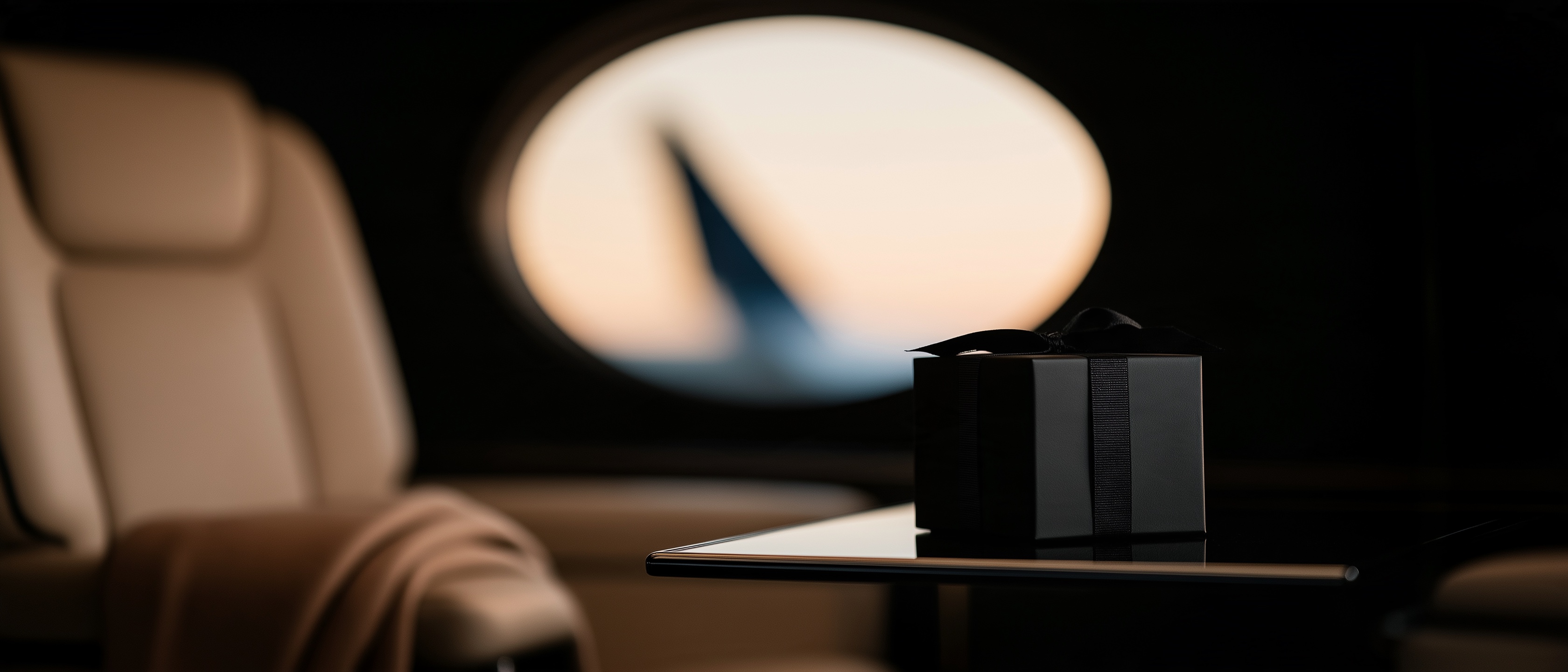 A black ribboned box on a table in a jet cabin, the wing in the window at dusk